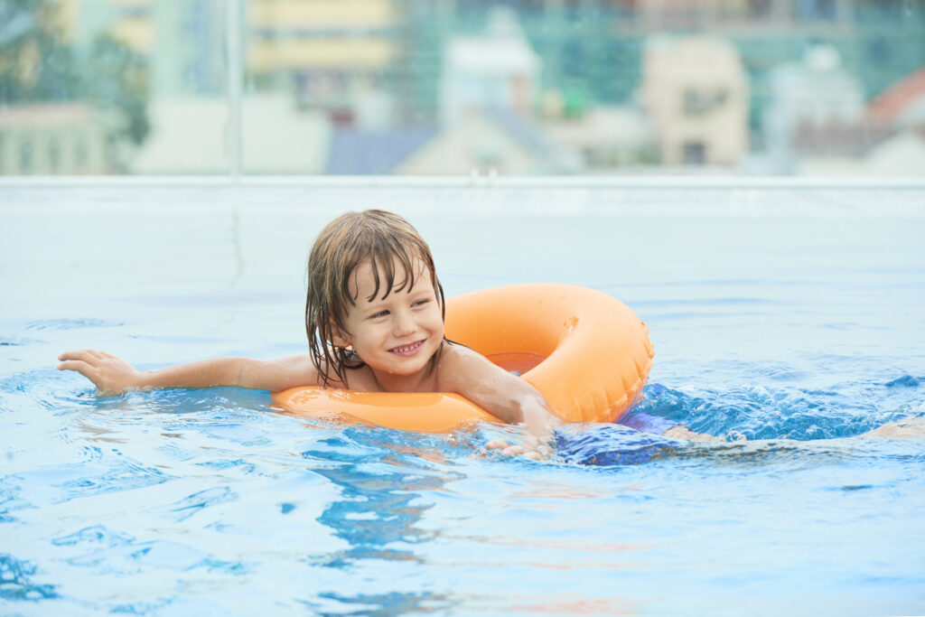 Happy little kid swimming in inflatable ring in swimming pool
